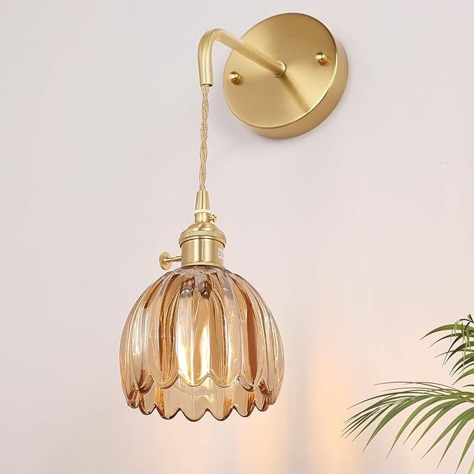 a wall light hanging from the side of a white wall next to a potted plant