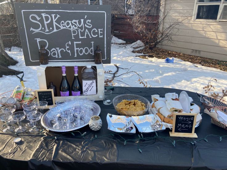 a table topped with lots of food and wine bottles next to a chalkboard sign