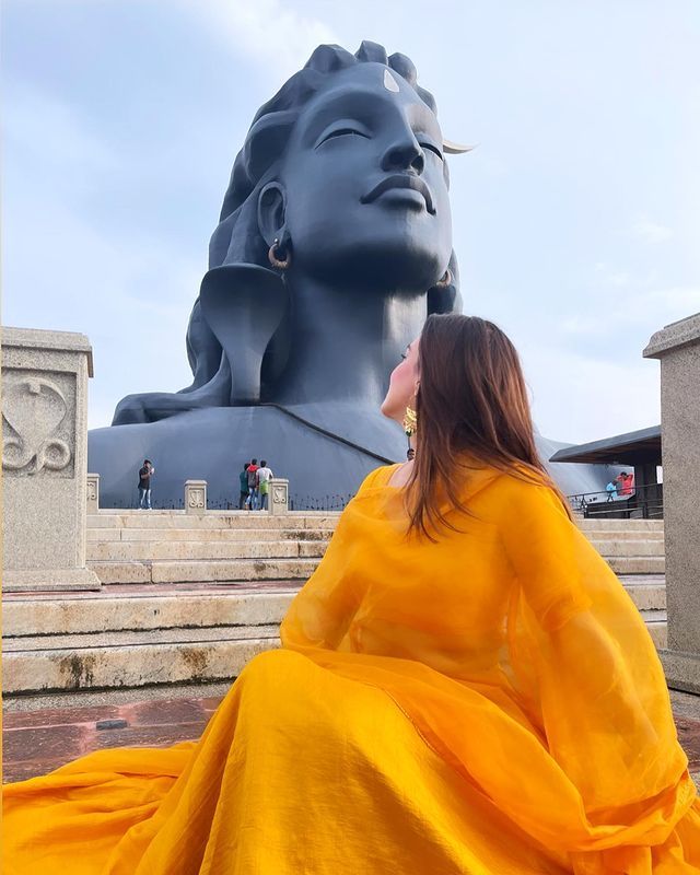 a woman in a yellow dress sitting on steps next to a large blue buddha statue