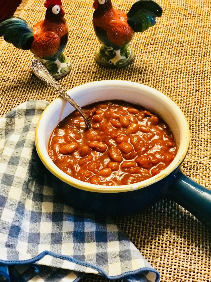 a bowl of baked beans with two chickens on the side