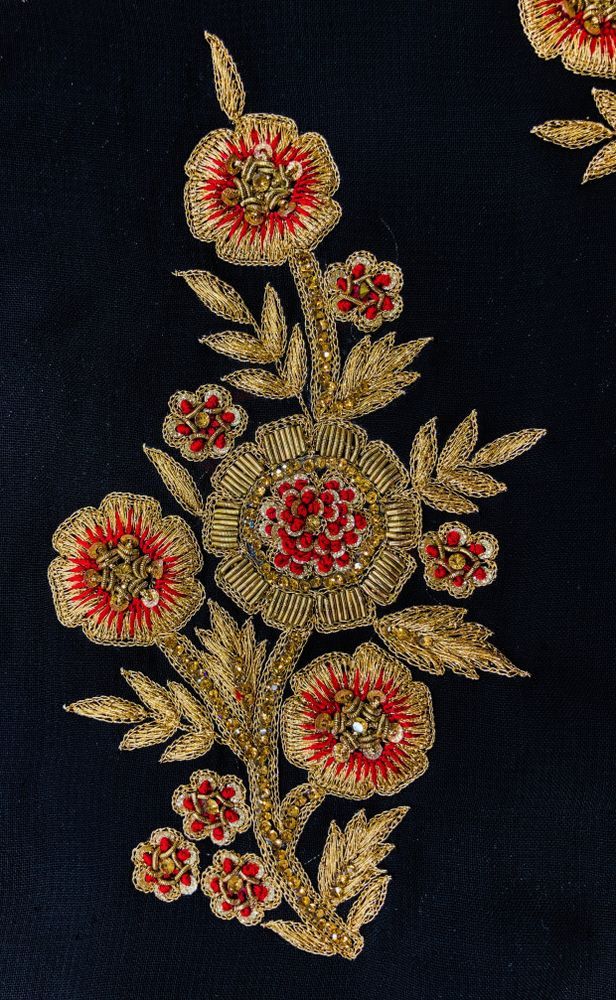 an embroidered fabric with red flowers and leaves on black background, closeup shot from above