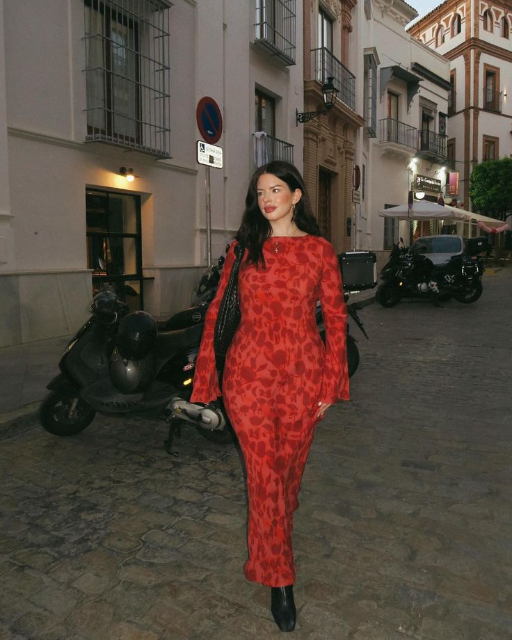 a woman in a red dress is walking down the street