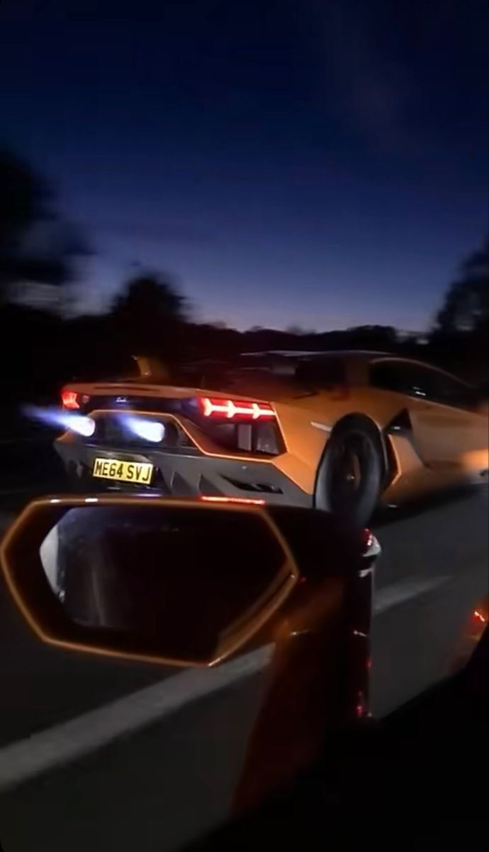 a yellow sports car driving down the road at night with its lights on and rear view mirror showing