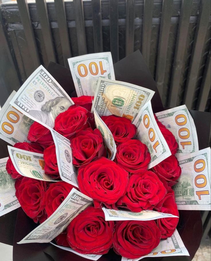 a bouquet of red roses sitting on top of a black box filled with hundred dollar bills