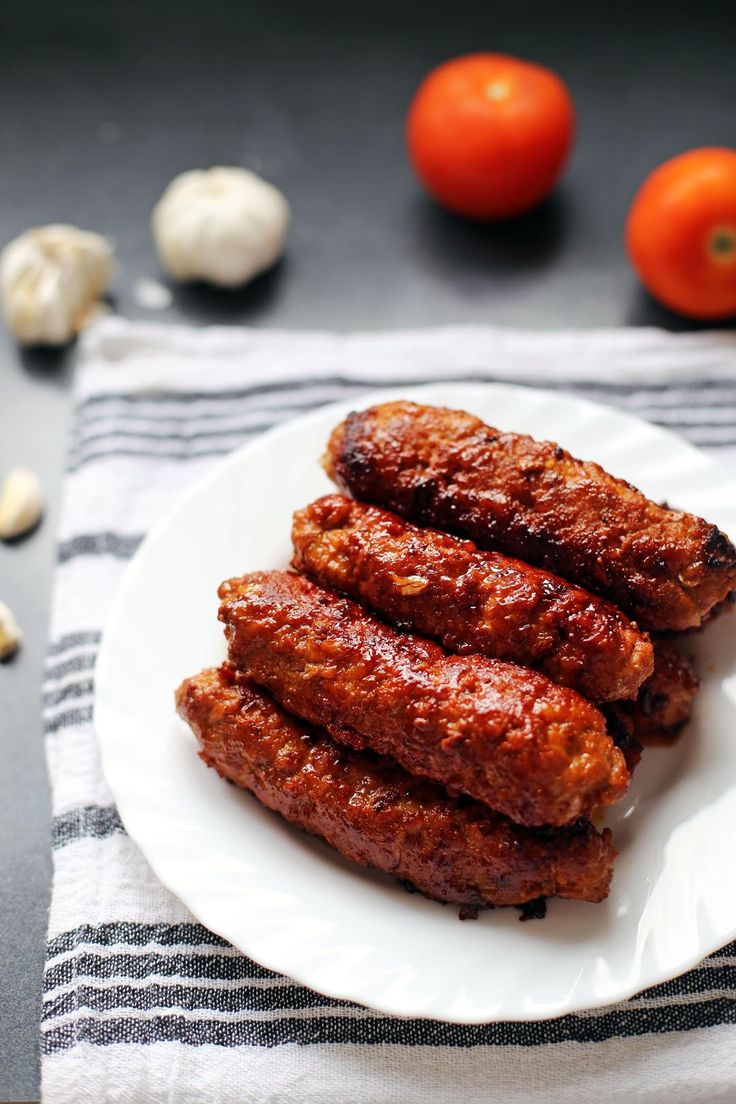 some meat on a white plate next to tomatoes and garlic