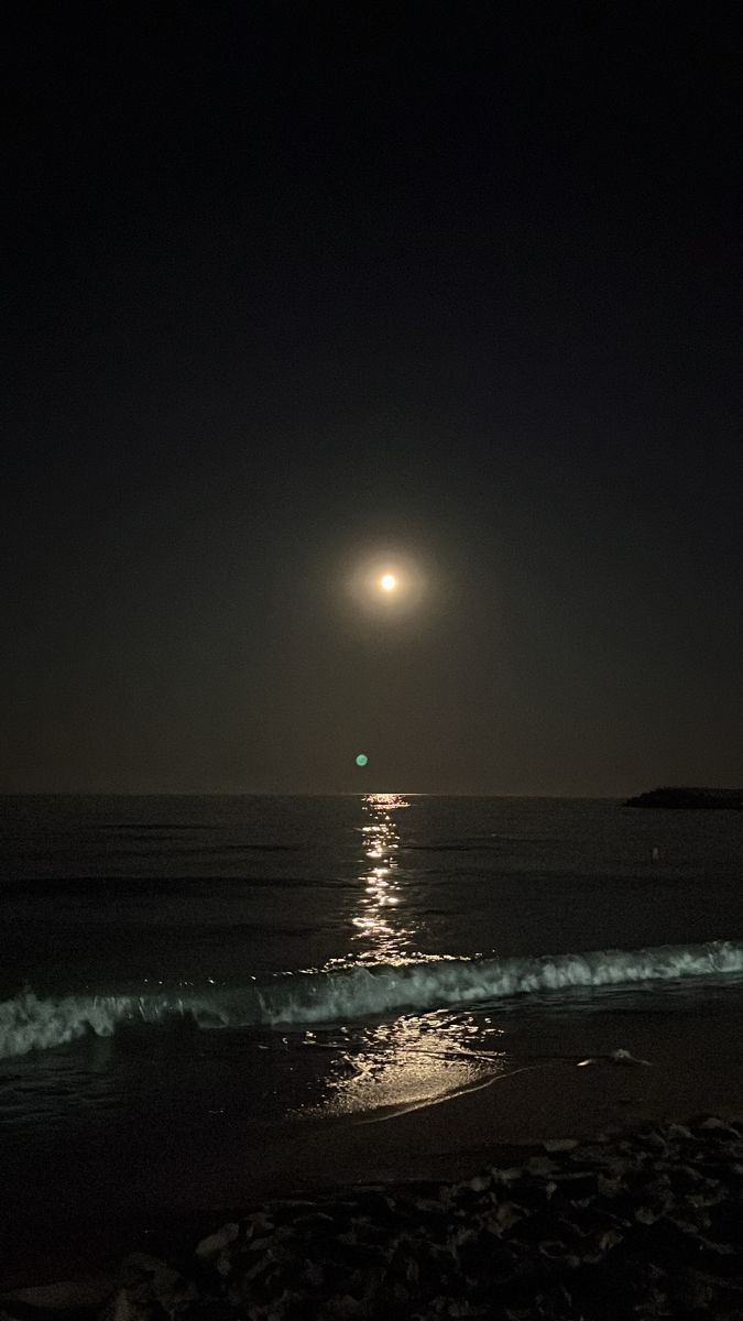 the moon is shining over the ocean at night