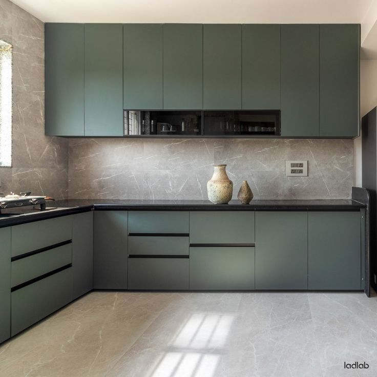 a modern kitchen with green cabinets and black counter tops, along with a white floor