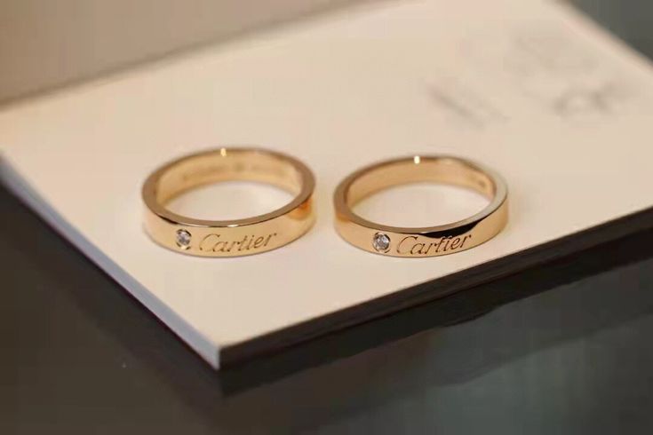 two gold wedding rings sitting on top of a white box with the word couple written on it