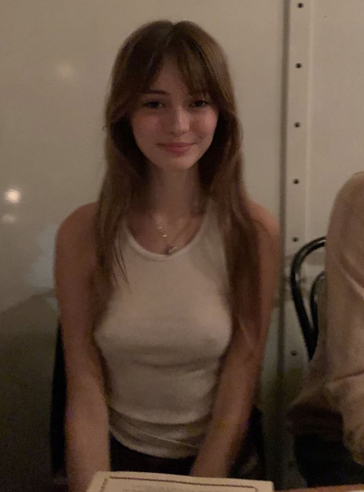 a woman sitting at a table with a pizza in front of her and another person behind her