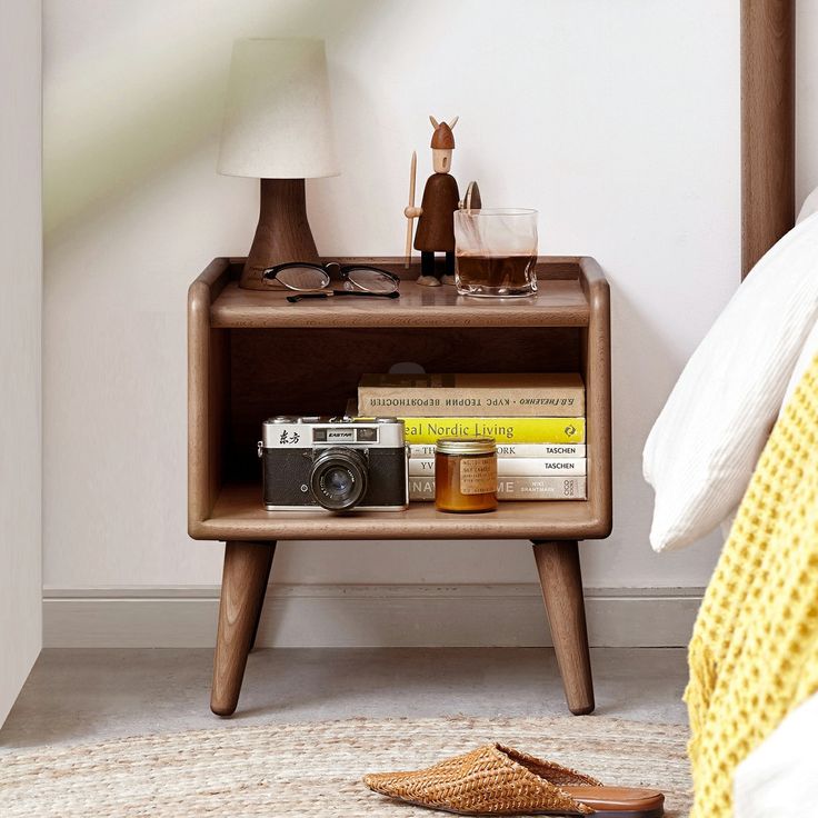 a nightstand with books, magazines and a camera on it