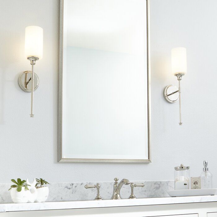 a bathroom vanity with two lights and a large mirror above it, in front of a white wall