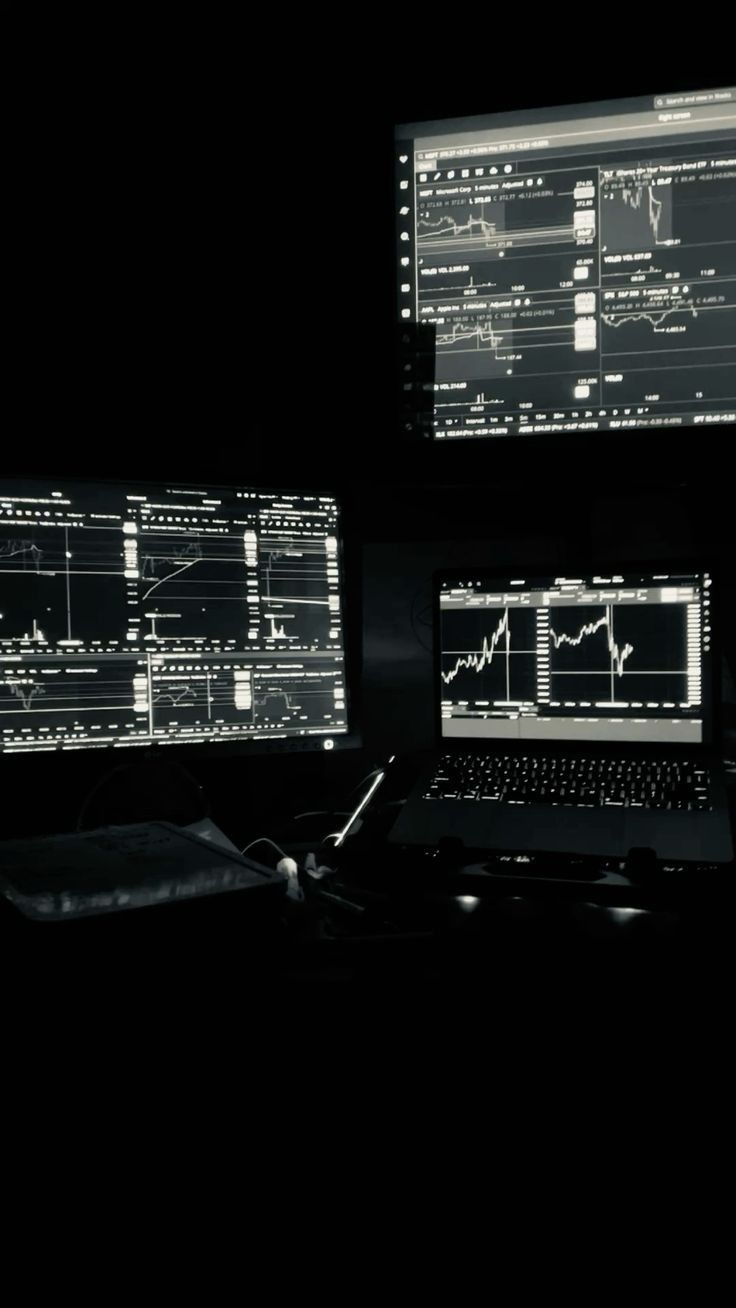 three computer monitors sitting next to each other on top of a black desk in the dark