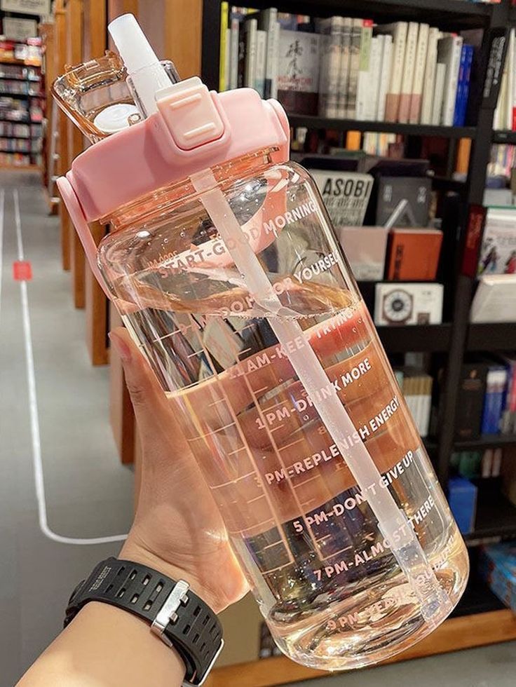 a person holding up a water bottle in front of a book shelf filled with books