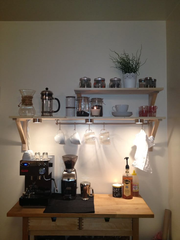 a coffee maker and some cups on a shelf above a stove top with light coming from behind it