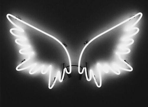 a neon angel wings sign hanging from the side of a dark wall with light bulbs on it