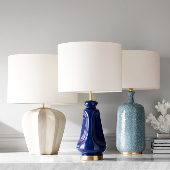 three lamps sitting on top of a table next to books and vases with flowers in them