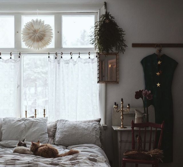 a cat laying on top of a bed in a bedroom next to a window with curtains