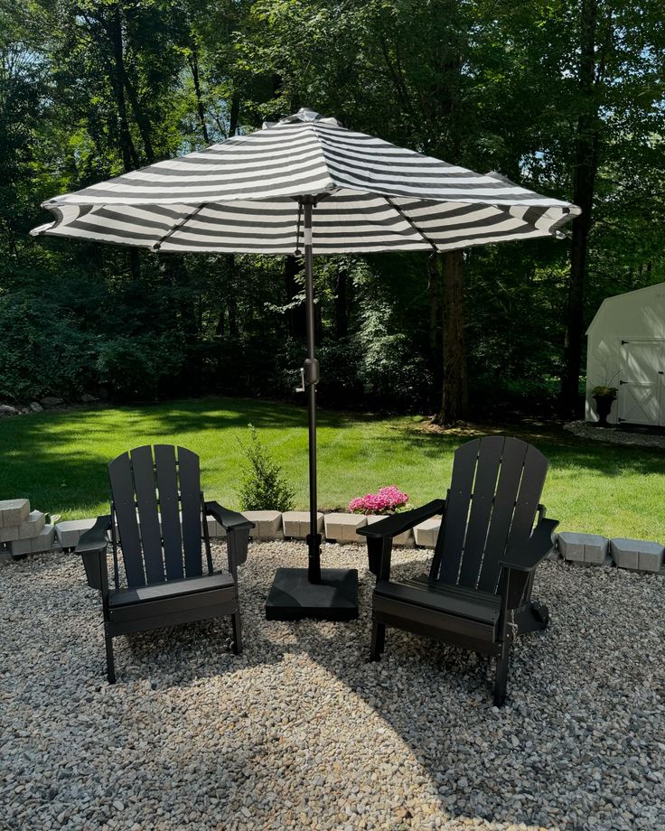 two chairs and an umbrella are sitting on the gravel in front of a lawn area