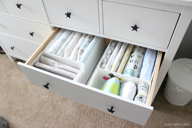 an open drawer with baby items in it on carpeted floor next to white dresser