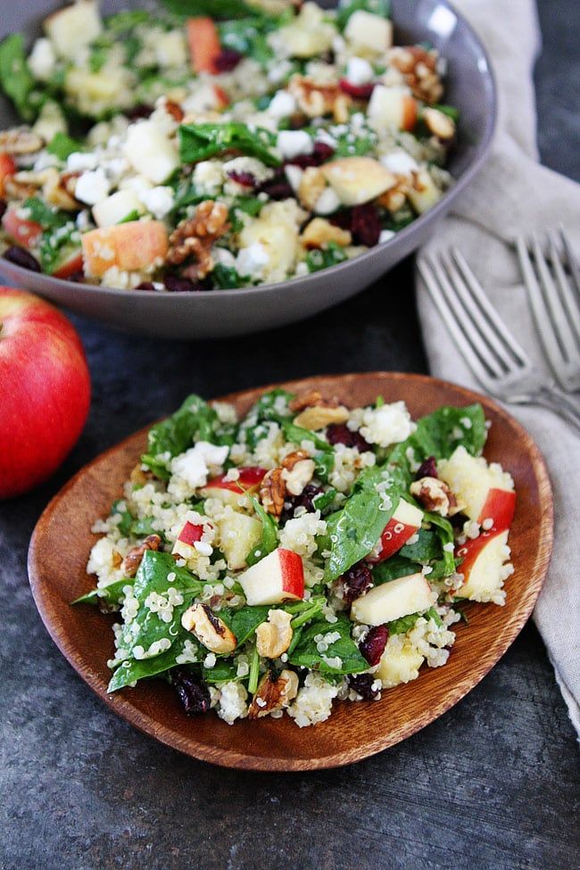 two plates filled with salad on top of a table next to an apple and silverware