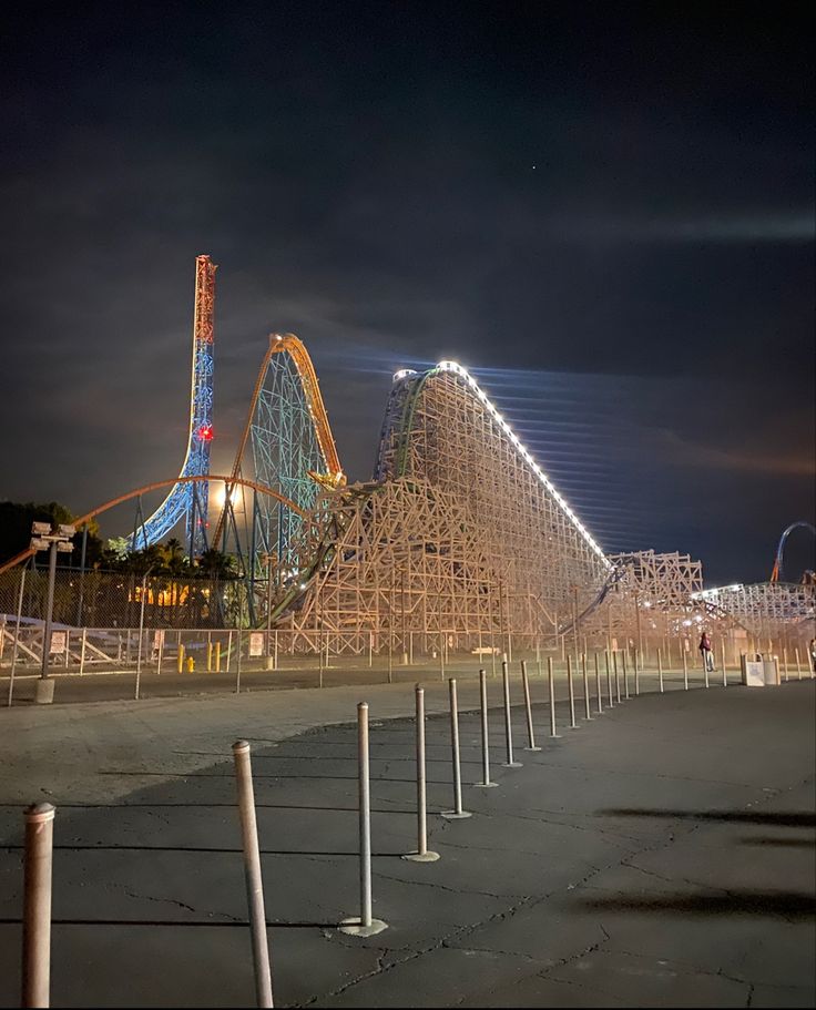 an amusement park at night with roller coasters in the foreground and lights on