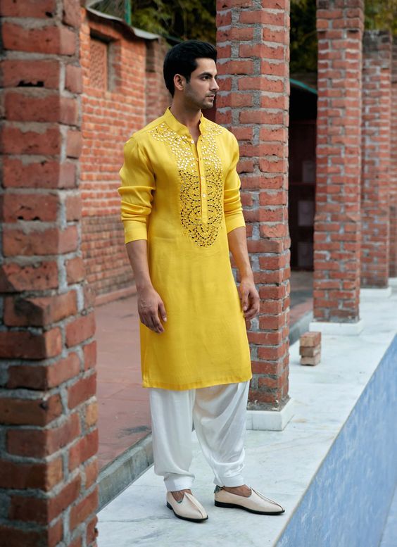 a man in yellow shirt and white pants standing by brick pillars with his hand on his hip