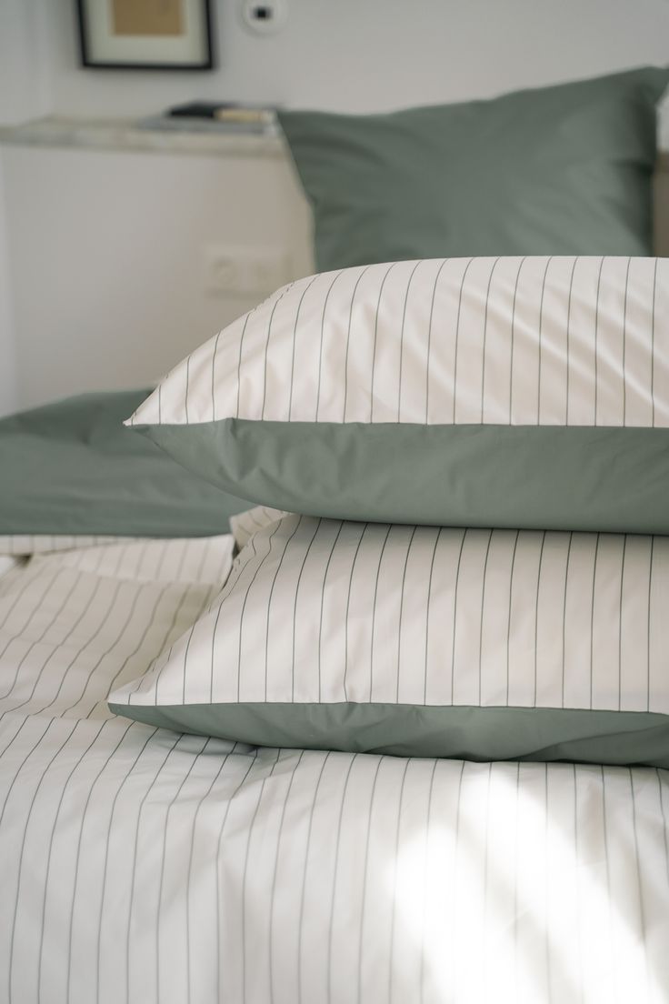 three pillows are stacked on top of each other in front of a bed with green and white sheets