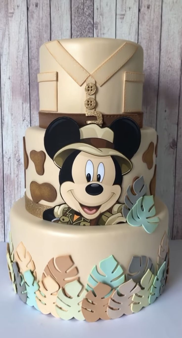 a mickey mouse cake is decorated with tropical leaves and an army uniform on top,