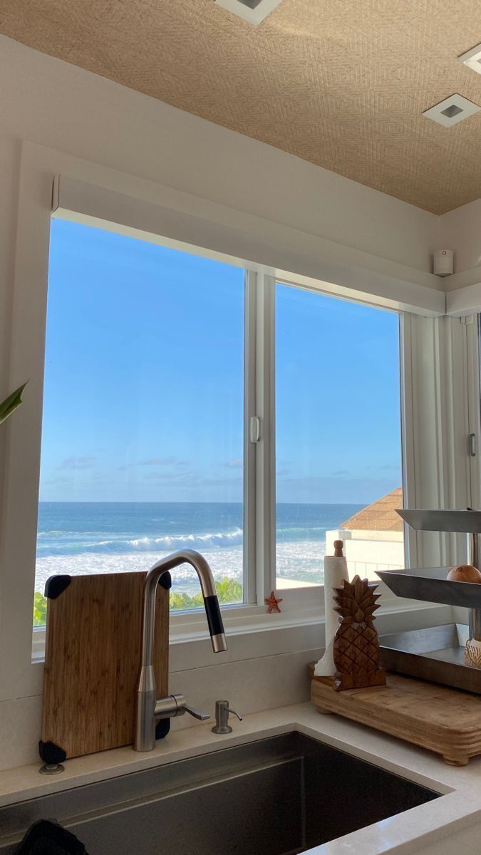 a kitchen sink sitting under a window next to a counter top with a cutting board on it