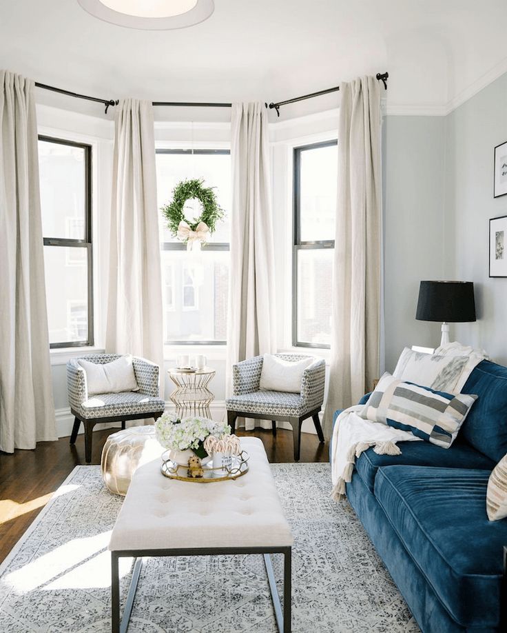 a living room with blue couches and white curtains on the window sill,