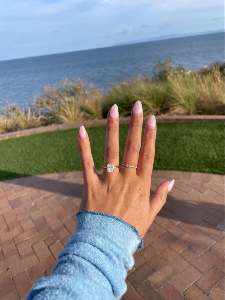 a woman's hand with a diamond ring on top of her finger near the ocean