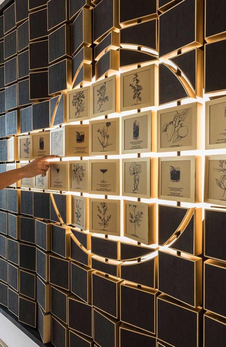 a woman pointing at an art piece on display in front of a wall with many framed images