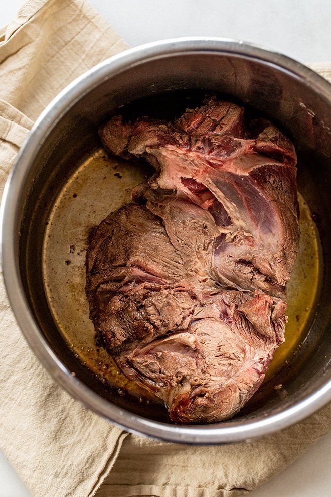 a pot filled with meat sitting on top of a table next to a napkin and fork