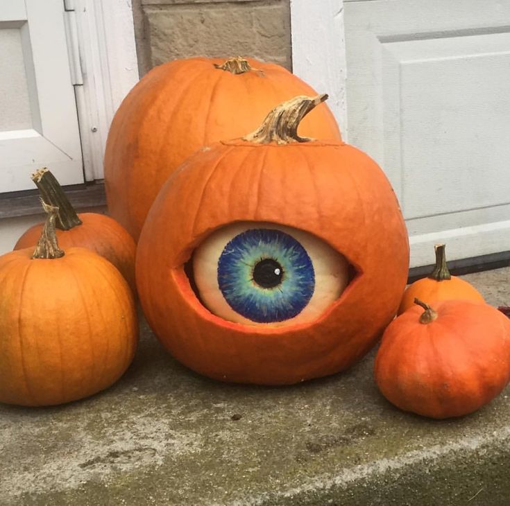 three pumpkins with an eye on them sitting in front of a door and two smaller pumpkins next to it