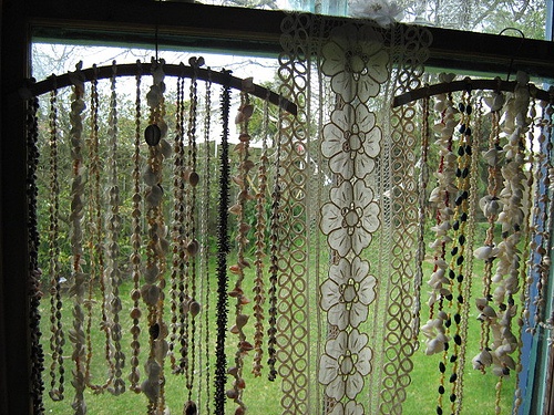 an open window with beads hanging from it's sides and on the outside, in front of a grassy area