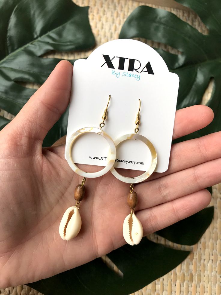 Material Shell, Wood Cowrie shells are back and reinvented in these neutral shell based hoops! These earrings are made with cowrie shells, wooden beads, and shell hoops to create the ultimate beach inspired earring that will pair with all of your spring and summer fashions. These earrings are a key piece in my summer collection which focused on natural, organic materials including shell, rattan, raffia, and wood.Please note that each pair is made to order and the shell hoops are made from genuin Neutral Earrings, Donuts Earrings, Accessory Inspo, Cowry Shell, Personal Jewelry, Summer Fashions, Bead Board, Cowrie Shells, Seashell Jewelry