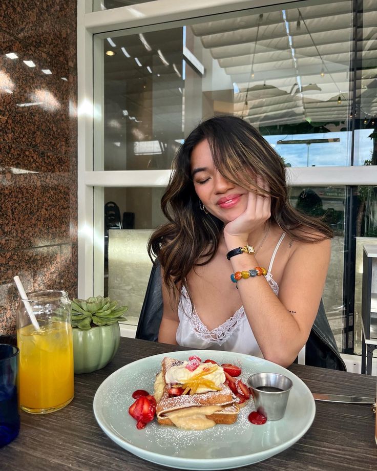 a woman sitting at a table in front of a plate of food with fruit on it