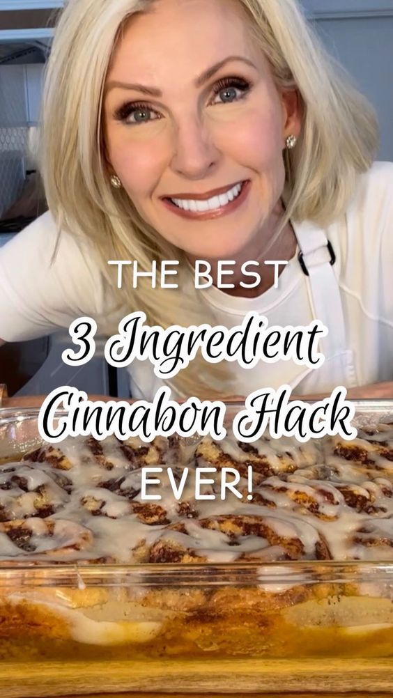 a woman with blonde hair and white shirt smiling in front of a baking dish filled with cinnamon flak