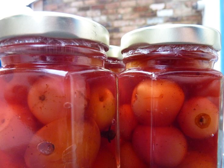 two jars filled with red fruit sitting on top of a table