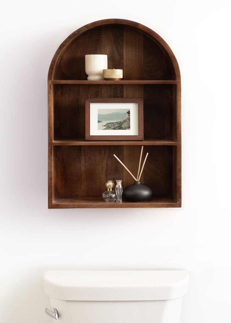 a wooden shelf above a toilet in a white bathroom with pictures and candles on it