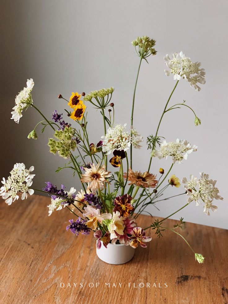 an arrangement of wildflowers in a white vase on a wooden table