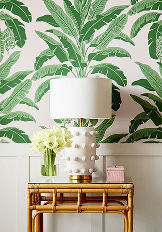 a table with a lamp on it next to a wall with green leaves and flowers