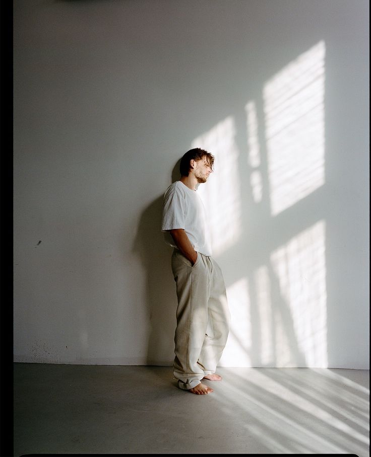 a man standing in front of a white wall with his head turned to the side