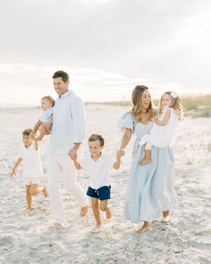 a family walking on the beach holding hands and smiling at the camera with their two children