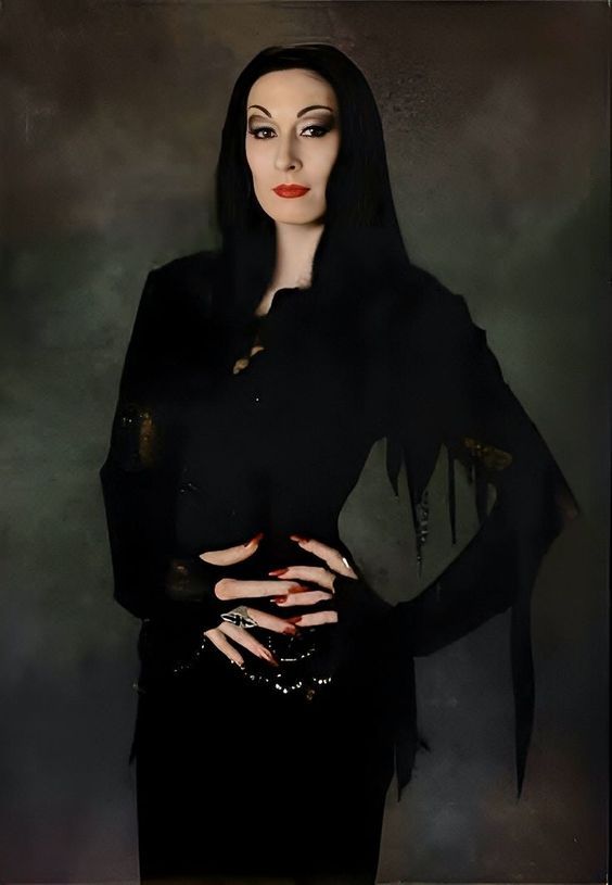 a woman with black hair and makeup is dressed in a dark dress, holding her hands on her hips