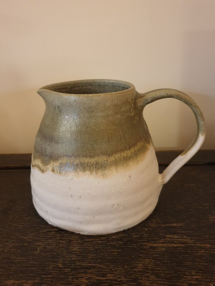 a brown and white ceramic pitcher sitting on top of a wooden table