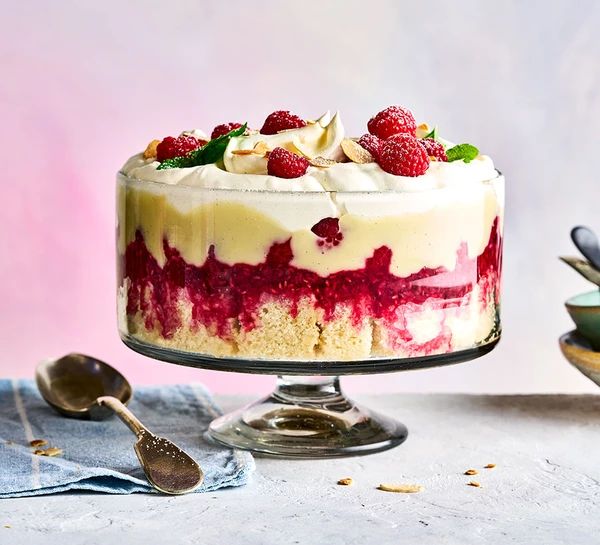 a cake with raspberries and cream is on a table next to other desserts