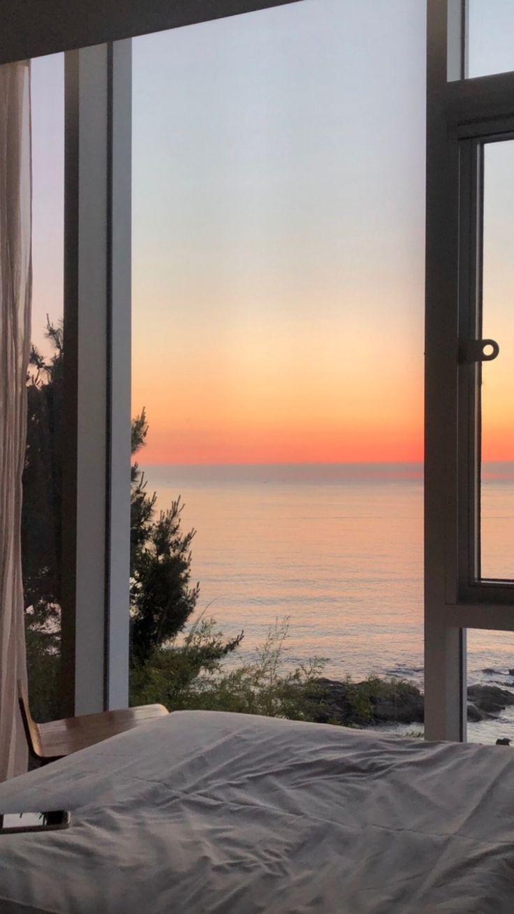 a bed sitting in front of a window next to a large window overlooking the ocean