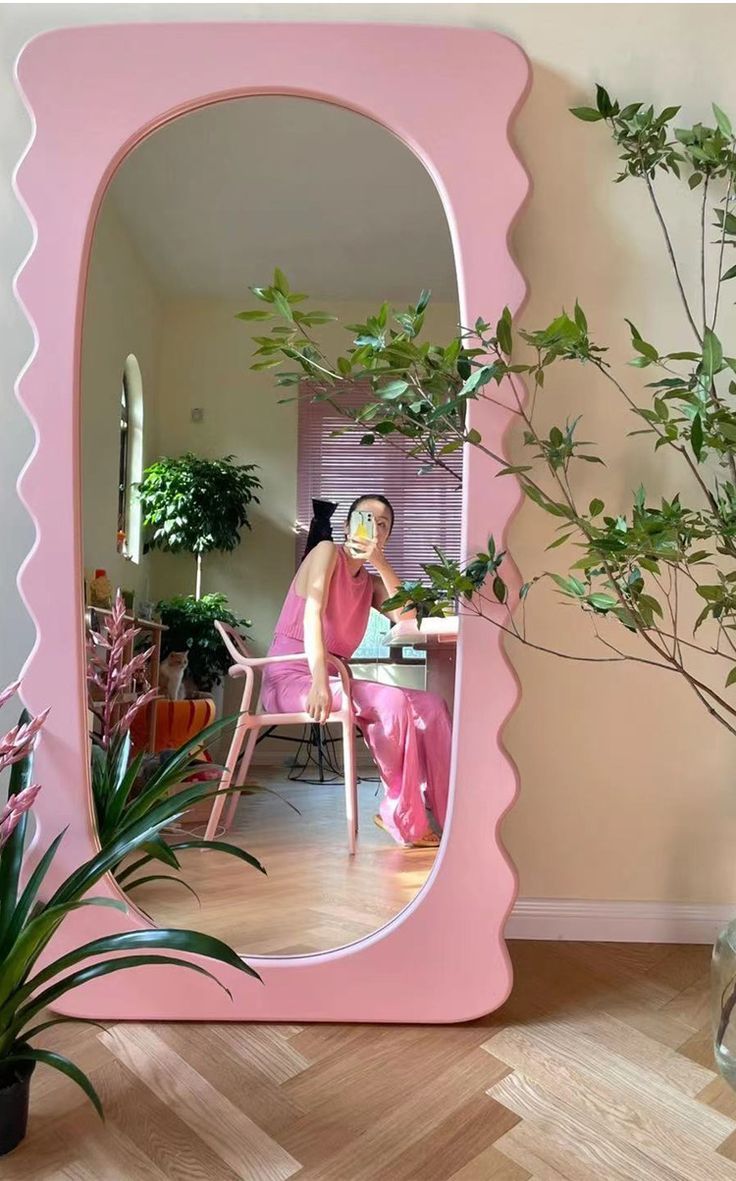 a woman sitting on a chair in front of a pink mirror with scalloped edges