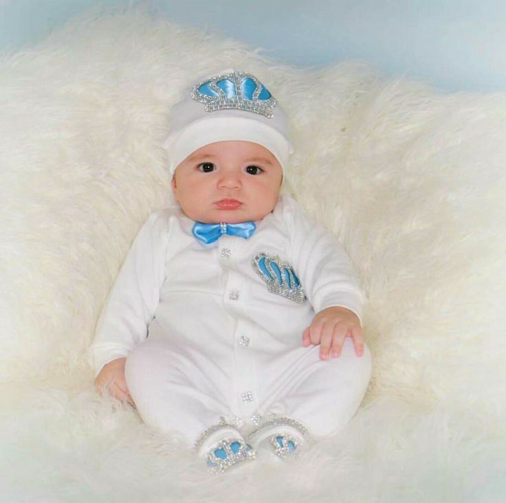 a baby wearing a white suit and blue bow tie sitting on a fluffy white blanket